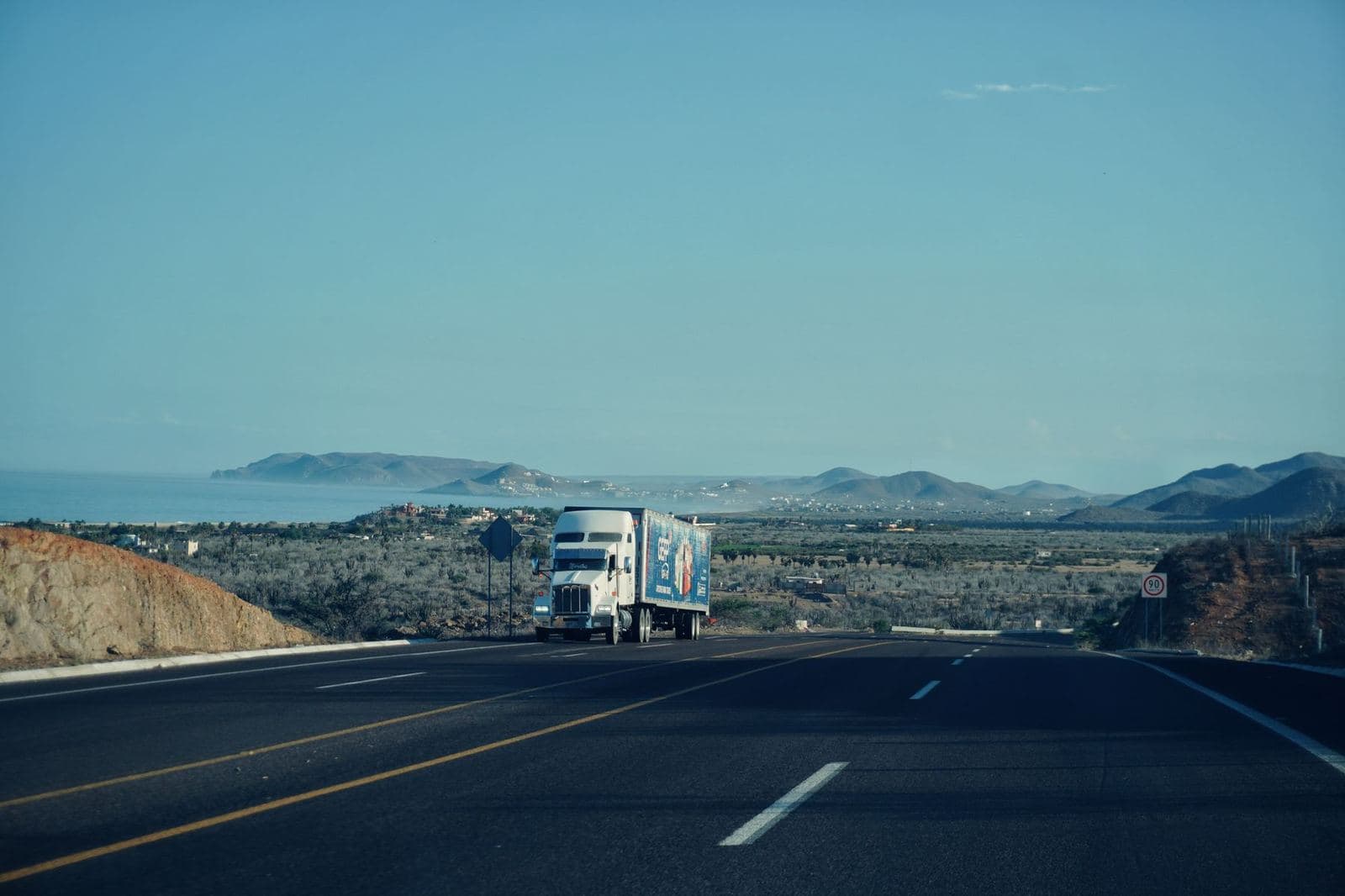 A semi truck on a scenic highway with mountains ahead, a planned lane